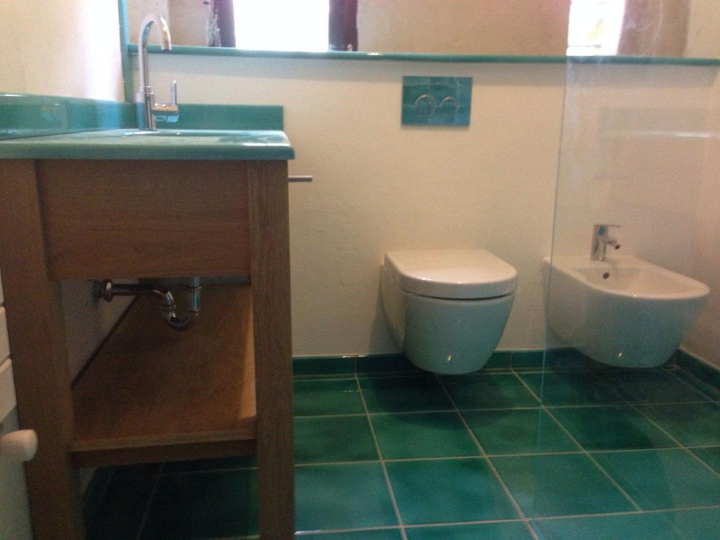 Salle de bains turquoise : plan vasque en verre, WC et bidet suspendus, sol carrelé vert