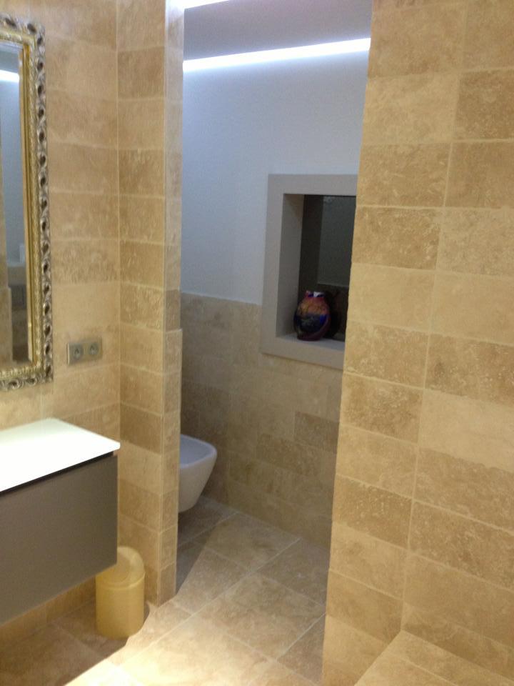 Espace WC séparé en travertin avec niche décorative et corniche lumineuse